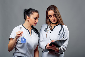 Two nurses discussing patient notes at grey background with test tube and folder. Medicine concept