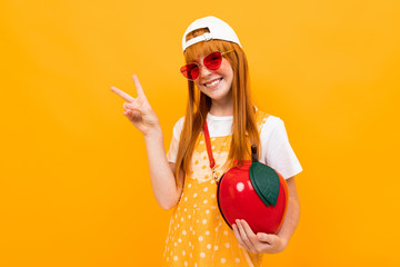 Pretty girl with red hair posing on camera smiles with little apple bag isolated on yellow background
