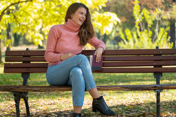 Young pretty woman sitting on a bench in a park and smiling.