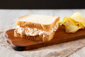 Delicious Homemade Pimento Cheese Sandwich with chips on a rustic wooden board, side view. Closeup.