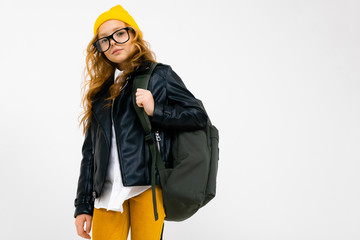 Teenager caucasian girl with yellow hat holds a big backpack in her hands isolated on white background