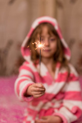 Happy small girl looking with admiration at burning sparkler in her hand over.