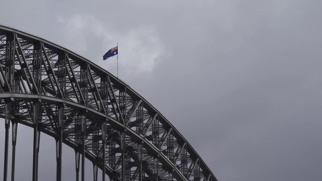 Sydney Harbour Bridge, Sydney, New South Wales, Australia - Australian Flag On Top Of The Bridge's Steel Railing Swaying In The Wind Under The Gray Cloudy Sky - Low Angle Shot