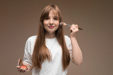 Obraz premium Caucasian girl in a white T-shirt with makeup brush on a dark background