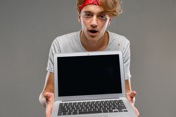 young man shows laptop screen with mockup on gray background