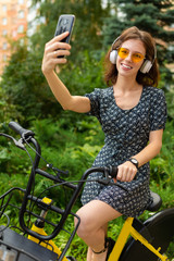 Fototapeta premium ecological transport concept. cute european girl rides a rental bike in the park and takes a selfie