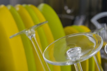 green and yellow clean plates and transparent glasses are in the dishwasher, side view, close-up