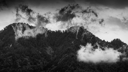 Panoramic view of low hanging white clouds in front of a mountain with dark moody sky