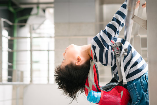 Little Asian hyperactive difficult boy hold handrail and lean body and head backwards, carry red backpack and insulated water bottle due to Autism, Behavioral and Attention Deficit Disorder.