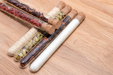 Various spices in glass flasks on a wooden kitchen table. Homemade spices ingredients for cooking, cardamom, coconut, cloves, star anise, goji berries. Copyspace for text.