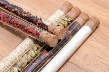 Various spices in glass flasks on a wooden kitchen table. Homemade spices ingredients for cooking, cardamom, coconut, cloves, star anise, goji berries. Copyspace for text.