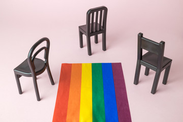 Small chairs and lgbt pride parade flag abstract on pastel pink background.