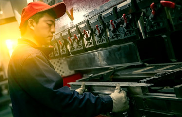 Asian worker using grinder to make heavy machine on assembly line