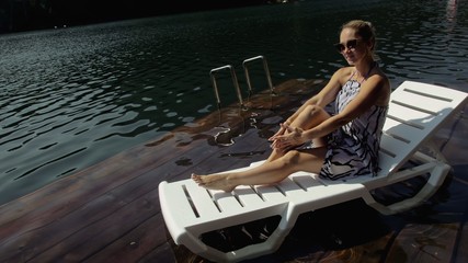 Woman lie on a sunbed in sunglasses and a boho silk shawl. Girl rest on a flood wood underwater...