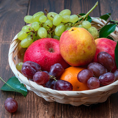 red grape berries and fresh fruits in a straw basket on a dark wooden background.