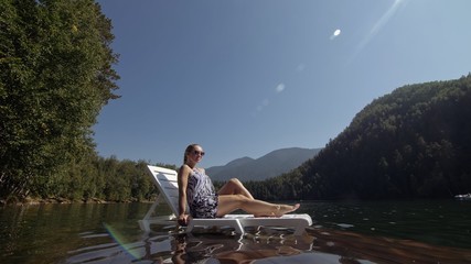 Woman lie on a sunbed in sunglasses and a boho silk shawl. Girl rest on a flood wood underwater...