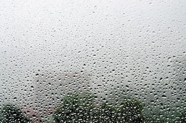 Raindrops on glass close-up. Background of trees and buildings outside