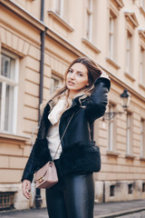 authentic street style portrait of european attractive woman wearing leather trousers and jacket, with studded ankle boots. crossing the street.fashion outfit details perfect for autumn fall winter
