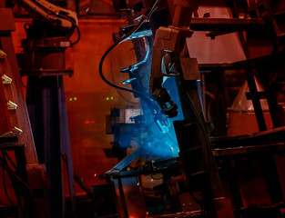 Large factory robotic arms are spraying sparks to weld car frames