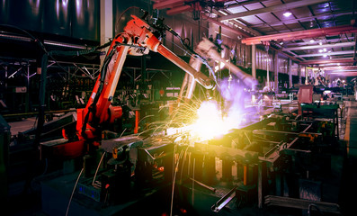 Large factory robotic arms are spraying sparks to weld car frames
