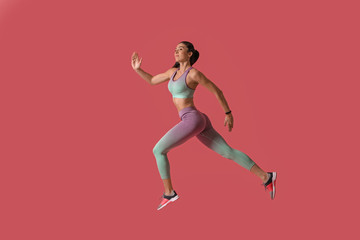 Fototapeta na wymiar Athletic young woman running on pink background, side view