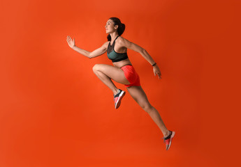 Fototapeta na wymiar Athletic young woman running on red background, side view