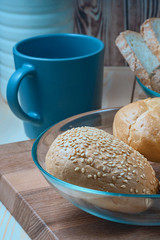 wheat buns with sesame filling in a glass bowl, a ceramic mug and a bottle of milk on the kitchen table