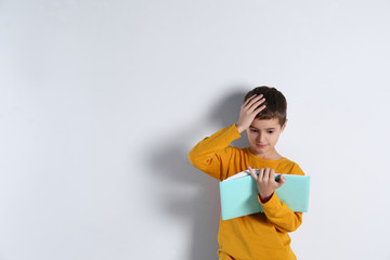 Cute little boy with book on light background, space for text