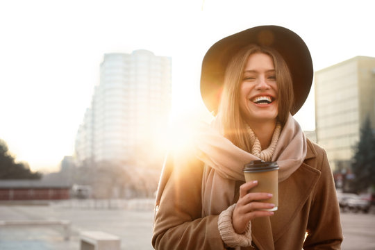 Young woman with cup of coffee on city street in morning