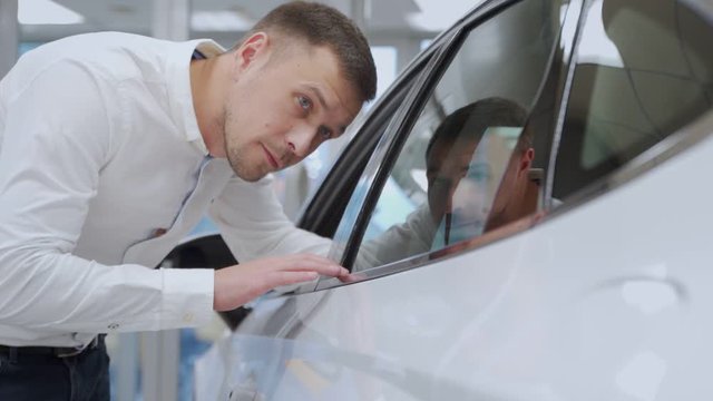 A man inspects his new car color. Auto business, car sale, technology and people concept - happy male with car dealer in auto show or salon.