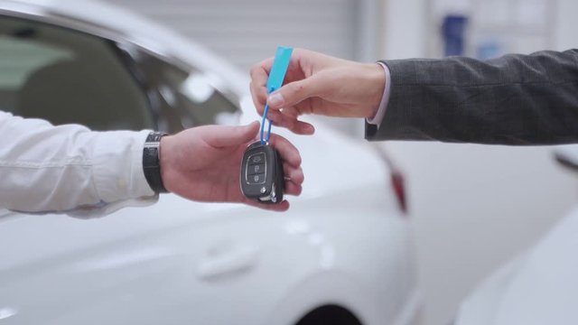 Car dealer handing over new car key to customer at showroom