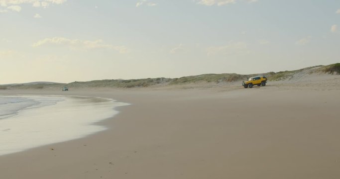 Yellow 4x4 on the beach at the historic four-wheel drive only access area of the exotic, fishing spot, Dark Point, Hawks Nest, NSW, Australia on a perfect summer day with waves rolling in