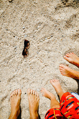 Fototapeta na wymiar family feet on a white dance on the sand around the painted sun
