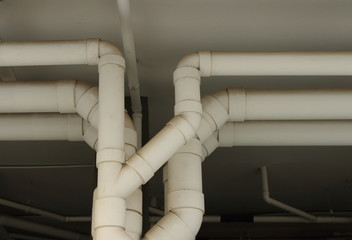 Closeup row of large plastic water pipes painted with white color run under ceiling of a building, selective focus 