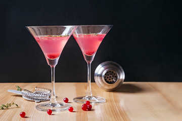 Two martini glasses filled with red color cranberry cocktail and barmen tools on the wooden table
