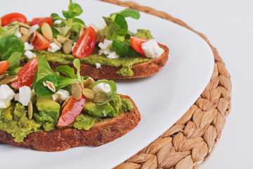 Two rye bread toasts with mashed avocado, tomatoes and feta cheese.