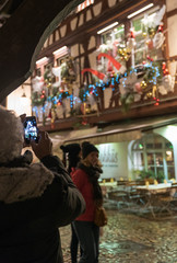 senior citizen taking a photo with cell phone  of beautifully decorated half-timbered houses in La Petite France in historic Strasbourg during the traditional Christmas market