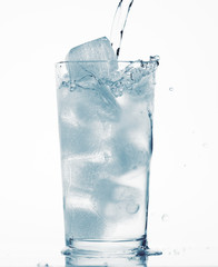 pouring water in a glass full of ice cubes, white background, blue toned object