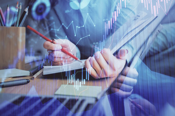 A woman hands writing information about stock market in notepad. Forex chart holograms in front. Concept of research. Multi exposure