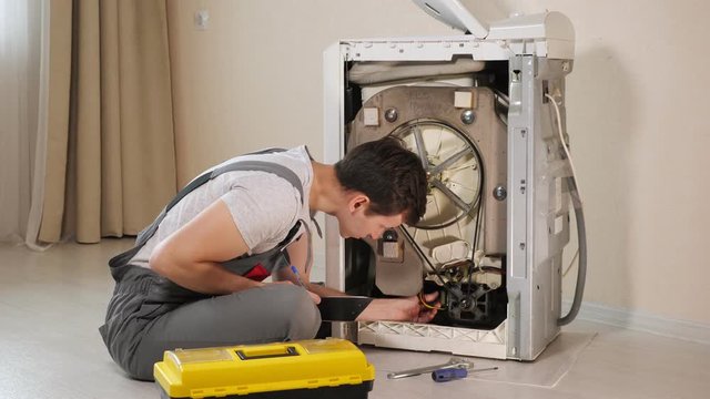 skilled repairman writes on clipboard checking broken washing machine top loader on floor in room closeup