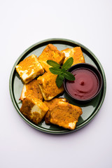 Amritsari Paneer Tikka made using cottage cheese cubes dipped in a batter made with besan, chat masala and spices and shallow fried in pan, served with ketchup
