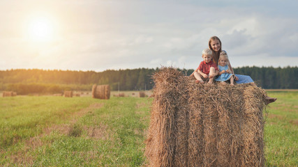A mother with two children sits on a sheaf of straw in a field.