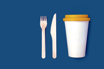Set of disposable wooden knife, fork and bamboo coffee cup on a blue background. The concept of...