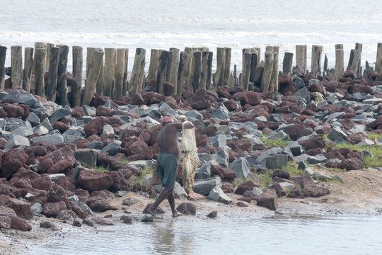 A fisherman walking with fishing net in beautiful and calm backwater beach in tropical Malabar Coast in the evening. Arabian Sea shoreline at distance. Marari Beach, Cochin Kerala India South Asia Pac