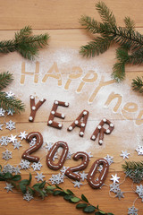 New Year's Eve background. Homemade chocolate cookies in shape of  2020 on a wooden table with pine branches and silver stars