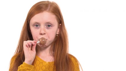 Close-up portrait shot of a lovely foxy haired girl with green eyes eating lollipop. Happy childhood concept