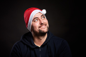 Smiling handsome young man in santa claus hat looks up. Black background. Close-up.