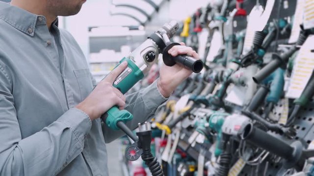 A young man chooses powerful drill in the hardware store