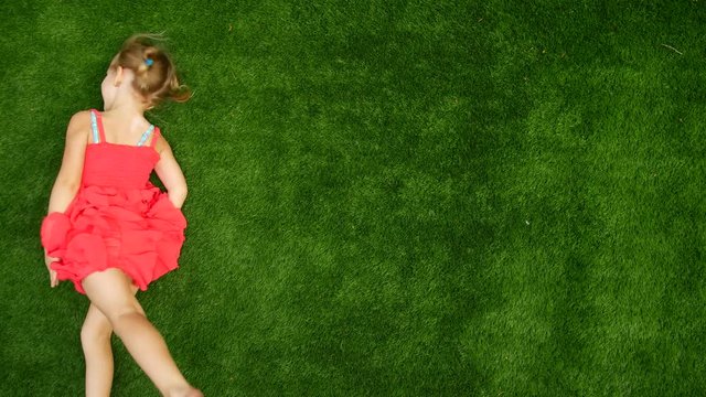 Girl child rides on the green grass. Walk in the fresh air, a girl rolls along the grass