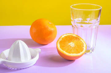 Oranges, a transparent glass and a juicer. Bright background, creative frame, fashion light.